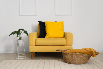 Yellow armchair with soft cushions and houseplant near white wall