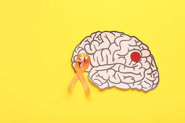 Paper brain and orange ribbon on yellow background. Multiple Sclerosis Awareness Month
