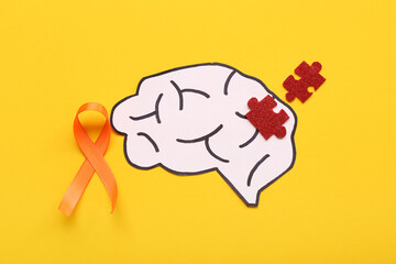 Paper brain with puzzle pieces and orange ribbon on yellow background. Multiple Sclerosis Awareness Month