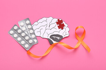 Paper brain with puzzle piece, pills and orange ribbon on pink background. Multiple Sclerosis...