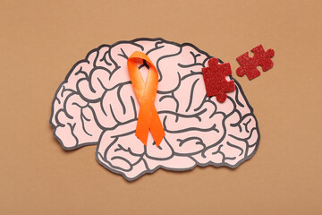 Paper brain with puzzle pieces and orange ribbon on brown background. Multiple Sclerosis Awareness...