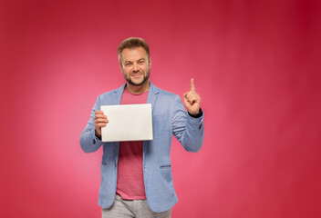 person holding a blank sign.Confident smiling man holding empty box and pointing with finger up on pink background.