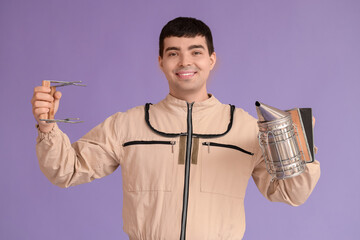 Male beekeeper with supplies on lilac background