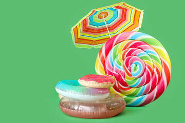 Inflatable rings, swimming mattress in shape of candy and beach umbrella on green background