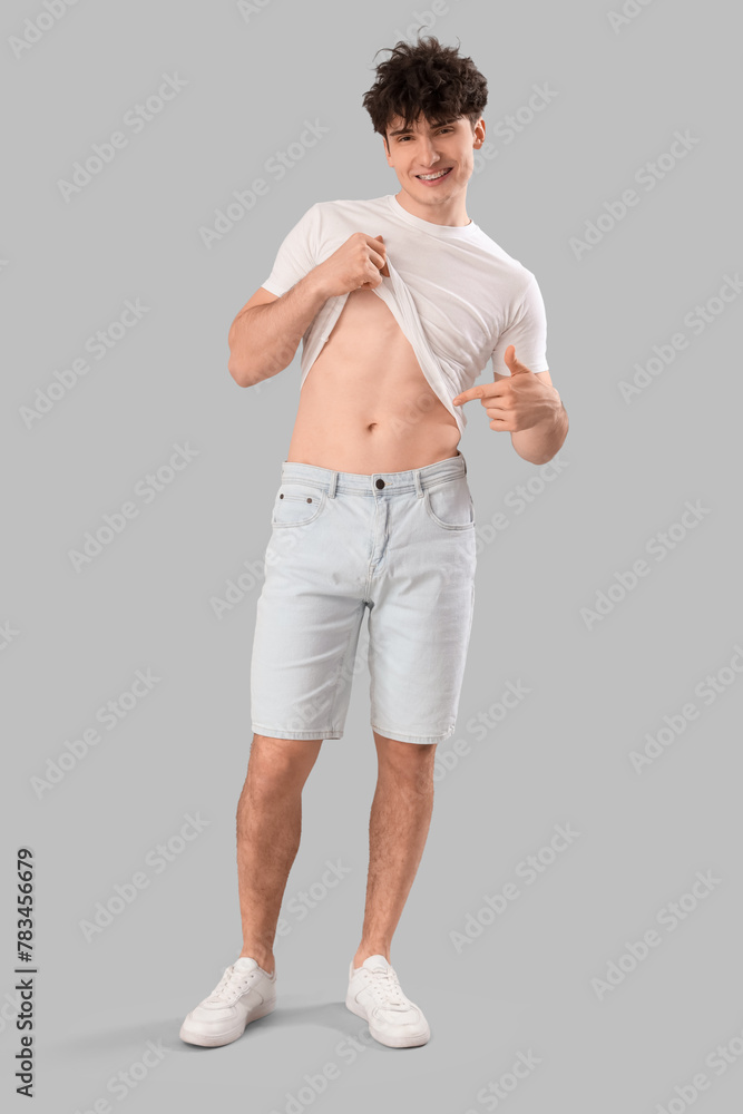 Poster Handsome young happy sporty man pointing at torso on grey background. Weight loss concept