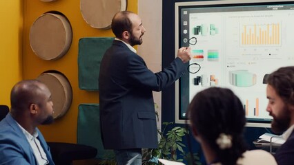 Project team reviewing monthly reports and data on interactive board, studying market trends and customer needs to ensure objectives fulfillment. Workers accomplish business goals. Camera A.