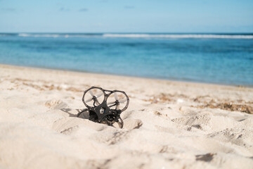 On the beach near the ocean there is an FPV drone lying on the sand, which lost its signal and fell down. The aerial drone is broken. Restoration and repair of electronics.