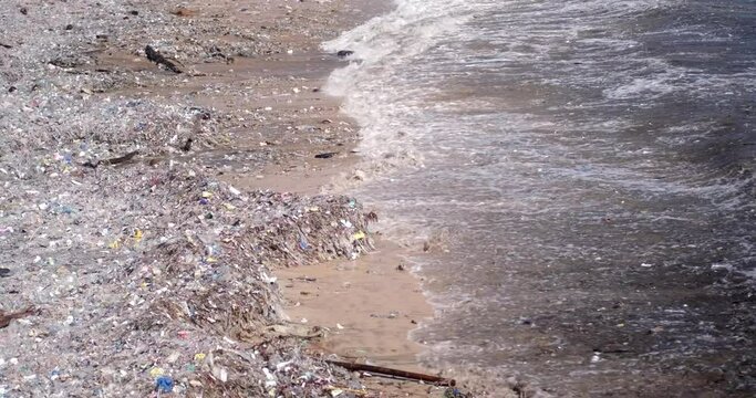 Sandy beach polluted with plastic waste. Global environmental disaster, mountains of garbage on the beach that came from the ocean. Waste floats in the water. Avoid bags and plastic bottles.