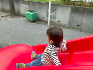 公園の赤い滑り台で遊ぶ子供