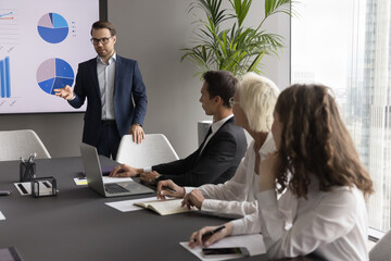 Diverse group of professionals, including male CEO engaged in formal meeting, with charts and...