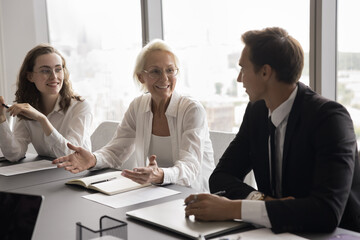 Positive mature woman trainer explain corporate goals at briefing, motivates team for successful...