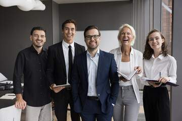 Five young and mature european professional team posing for photo in boardroom, gathered together...
