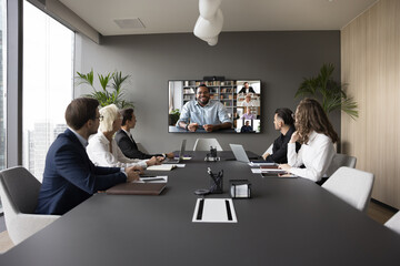 Group of businesspeople gathered in conference room take part in virtual meeting with international...