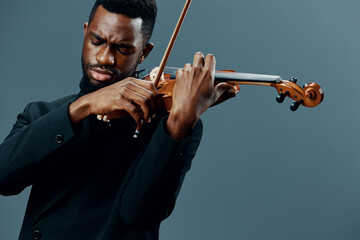 Elegant African American man in black suit playing violin on gray background in classical music...