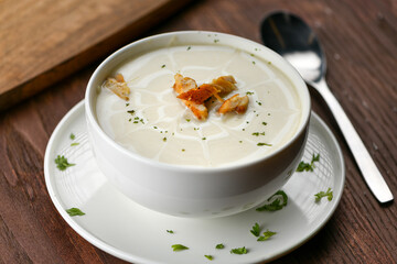 A bowl of hot cream chicken soup decorated wit parsley and vegetables on a wooden table.
