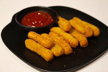 Chicken crispy finger fries with a bowl of tomato sauce in a black ceramic plate, ready for serving