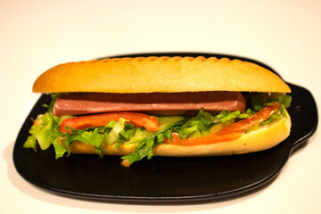 Hotdog sandwich with lettuce and tomato in a black ceramic plate