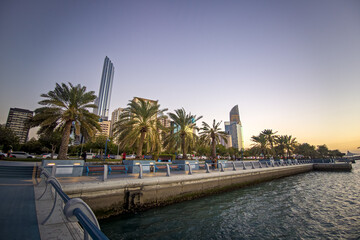 Strolling along the Abu Dhabi Corniche, a scenic waterfront promenade with stunning views of the Arabian Gulf and city's iconic skyscrapers - obrazy, fototapety, plakaty