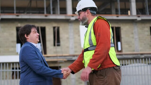 Banker client meeting with foreman at construction site shaking hands greeting and concluding a new deal on a real estate construction agreement.