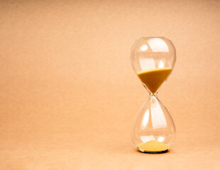 Hourglass on light brown recycled paper background with copy space. Golden sand in sandglass clock isolated on eco kraft paper background. Time, timer countdown, deadline watch.