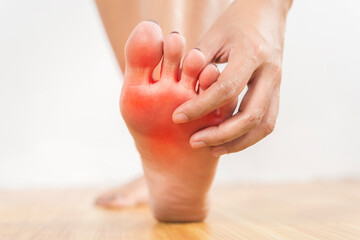 A person is touching their foot, which is red and swollen.