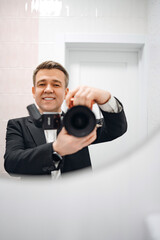 Male photographer in a business suit taking selfie with camera in reflection.