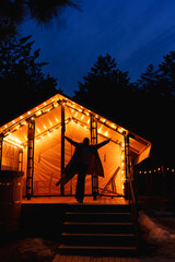 Glamping from tent houses in the forest in the dark. silhouette of a woman 