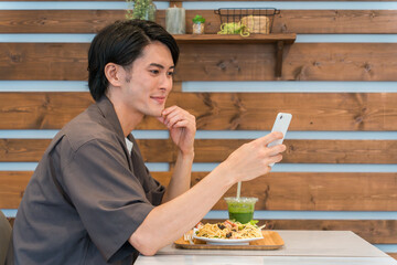 カフェで食事中にスマホを使う若いアジア人男性（ながらスマホ）
