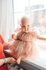 Cute little girl in a fluffy fancy pink dress sitting on the windowsill 