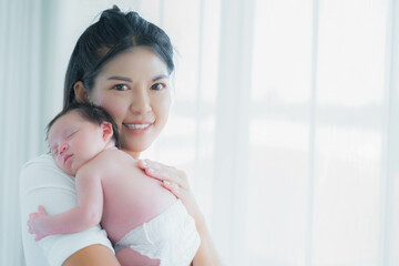 A serene moment as a young mother tenderly holds her sleeping newborn baby in a brightly lit home.
