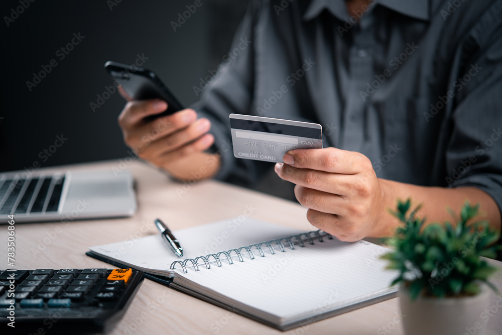 Poster man with credit card and smartphone finalizes a transaction, with a calculator and notepad nearby. o