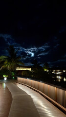 A beautifully illuminated path in Fiji under a dramatic cloudy night sky, creating a serene and mystical atmosphere. The soft lights guide the way, contrasting with the dark, moody clouds above