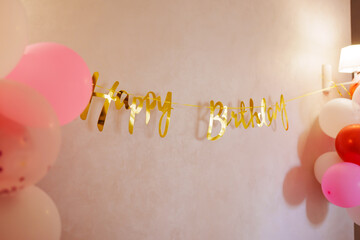 the color is golden Happy Birthday lettering on the wall with balloons. 