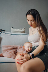 Cute baby daughter in an elegant dress lies on her mother's knees