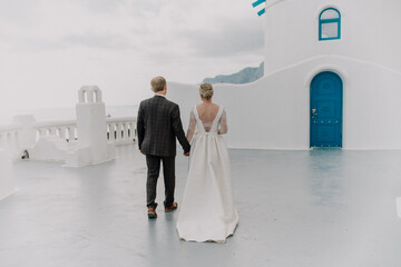 A bride and groom are walking down a path in front of a blue door. The bride is wearing a white...