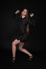 Fashion model with long legs. Full length portrait is set against black background. Sensuality blond with long hair is wearing black short transparent dress, felt hat with wide brim, high heeled shoes