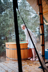 Laughing woman in bathrobe at the font for bathing in the forest. hot tub