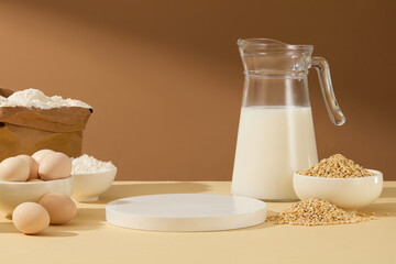 Blank space for presenting product with white round empty podium, decorated by some baking ingredients, a glass bottle of fresh milk, soybean, flour contained in bowl and paper bag, some eggs. 