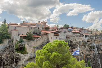 A historic monastery perched atop a rocky cliff with a Greek flag in Meteora Greece