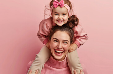 Obraz na płótnie Canvas A happy mother is carrying her daughter on the shoulders, laughing and having fun together isolated over pink background with studio light in pastel colors