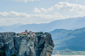 Stunning cliff-top monastery against a mountainous backdrop and clear blue skies in Meteora Greece