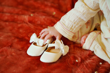 The little girl is holding small white shoes with bows in her hands.