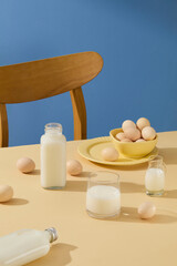 Fototapeta na wymiar Advertising photo with eggs and milk on blue background. Milk is contained in glass cup and bottle, eggs arranged on table. Scene suitable for food or beverage products
