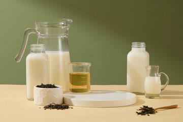 Blank empty white podium for displaying products, decorated by some glass bottles of milk, tea and tea leaves. Beverage concepts for designing