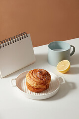 An attractive cinnamon Roll has some flour on surface is placed on a round dish with a cup of fresh milk and calendar on table. Minimalist scene for cooking products