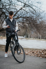 Fototapeta premium Young male teenager outside having a break on bike ride while checking his smart phone