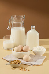 Brown and beige tone with a set of ingredient baking, a unlabeled glass bottle of soy milk beside many other ingredients such as eggs, flour, soybean. Photo with blank space 