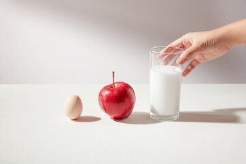 Front view of an egg, an apple and a glass of sweetened milk is touching by woman hand in the...