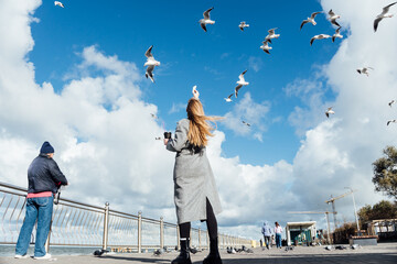 Young woman feeds seagulls. Сoastline scene with girl. Concept of travel