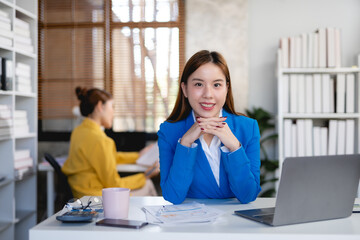 Professional young asian businesswoman in blue blazer posing confidently at office desk. Young...